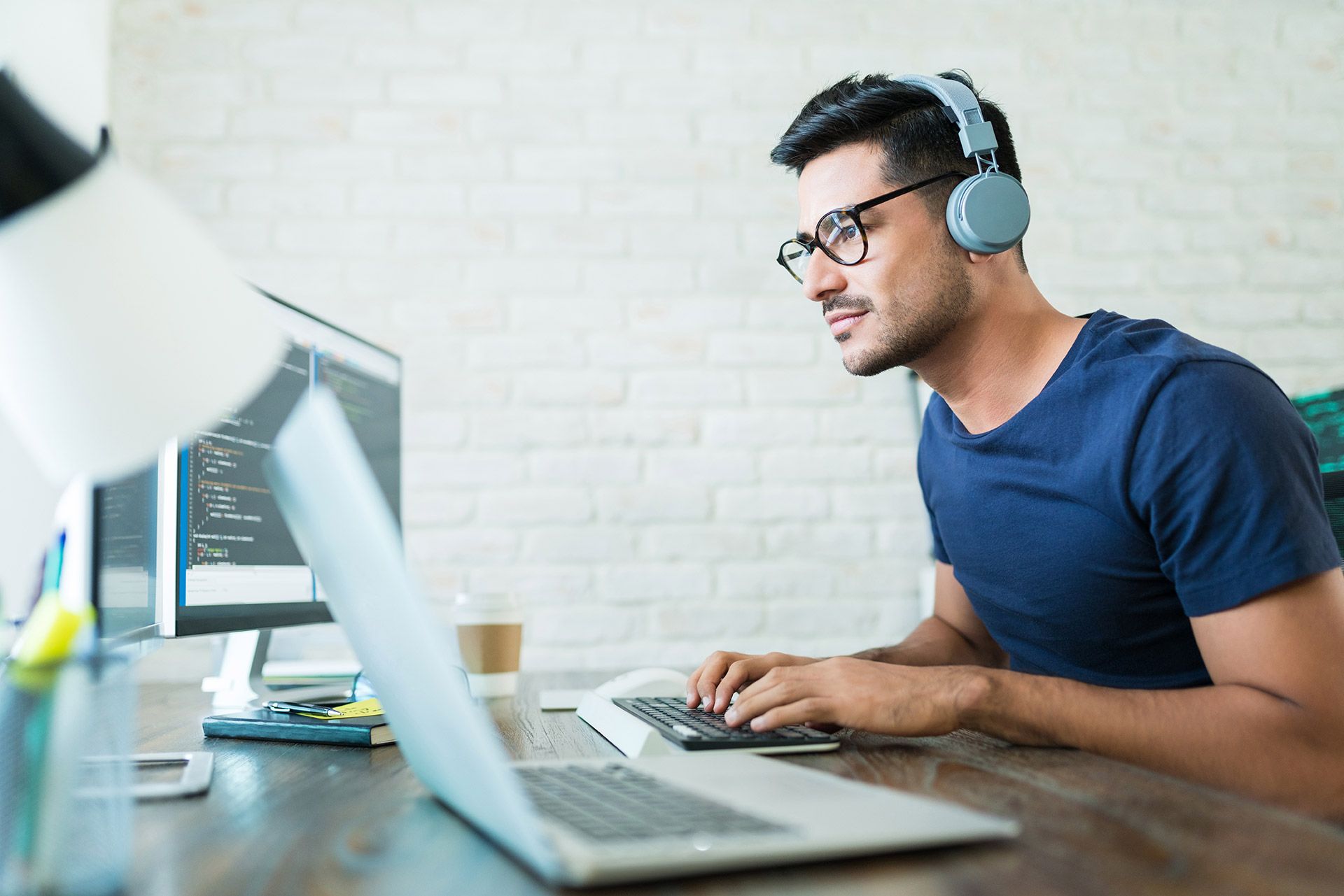 A man with headphones sits at a desk, focused on his laptop while working.