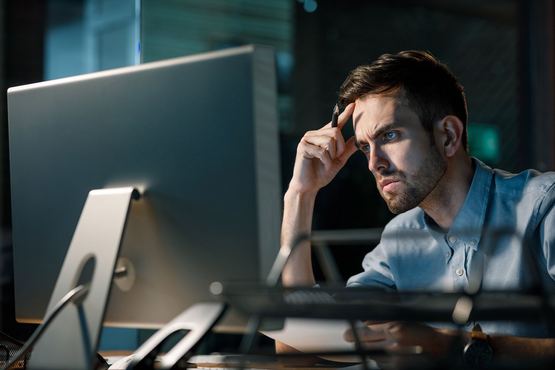 A man at a desk, leaning his head on his hand, suggesting fatigue or deep concentration.