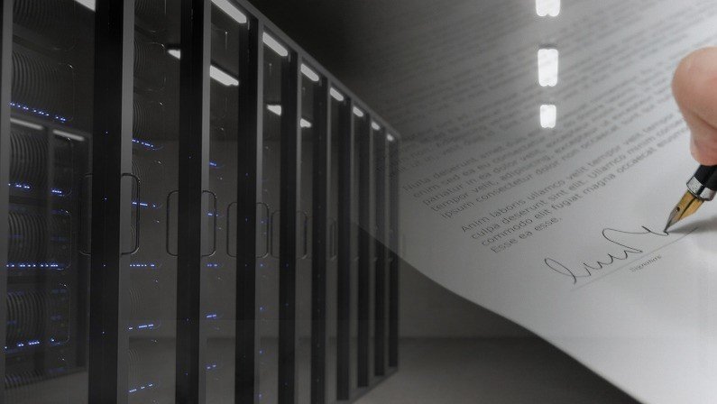 A hand holding a pen and a server room filled with racks of servers and blinking lights.