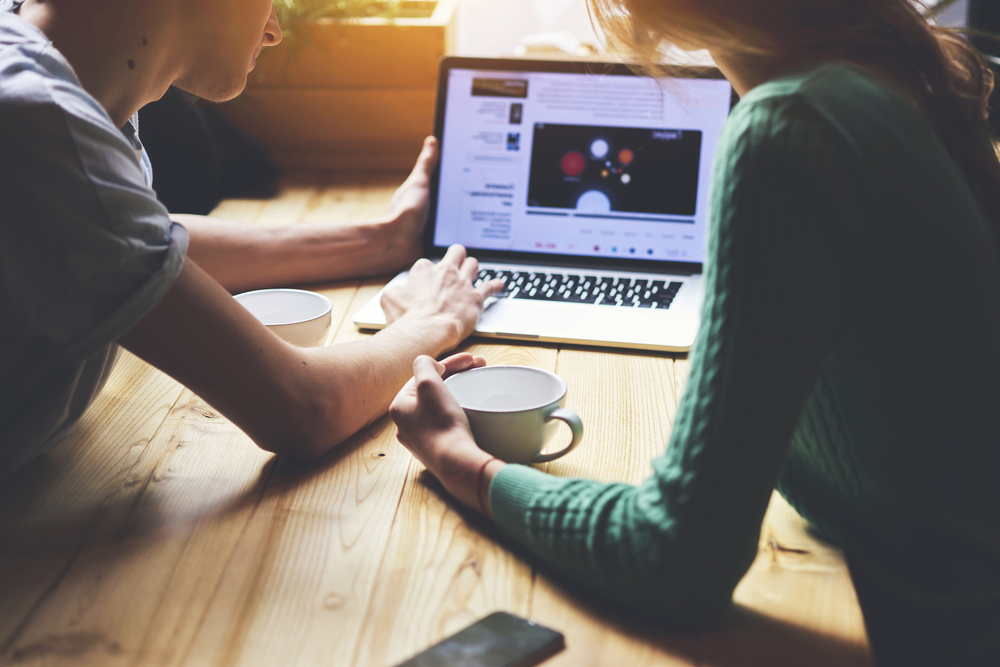 Two individuals seated at a table, collaborating on a laptop together.