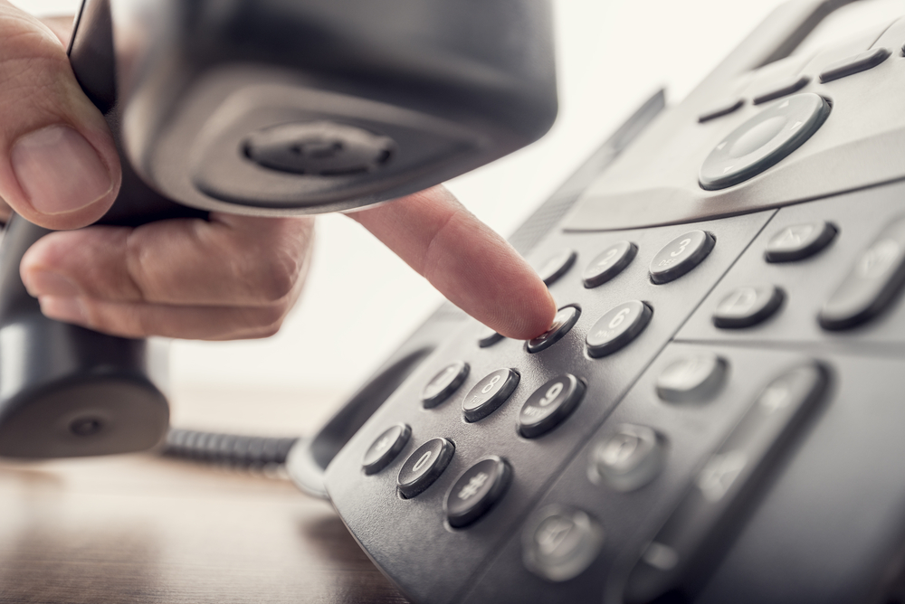 A person pressing a button on a telephone, focusing on the action of dialing or answering a call.