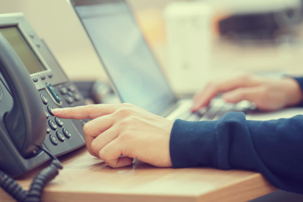 A person is using a telephone while seated at a desk, focused on a conversation.