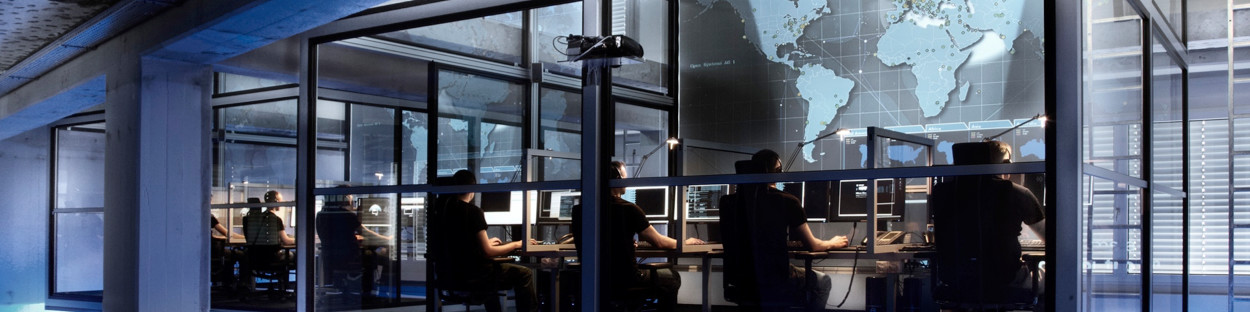 A large glass wall in an office, with people working on computers.