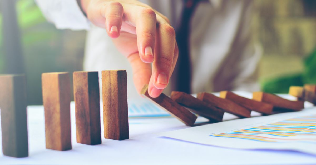 A businessman’s hand pushes wooden blocks to construct a dominoes board, illustrating strategic planning and focus.