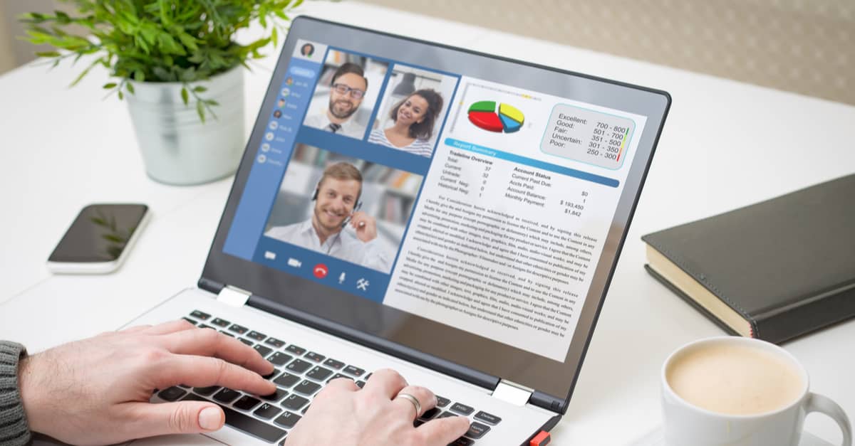 A person typing on a laptop displaying a video call with multiple participants visible on the screen.