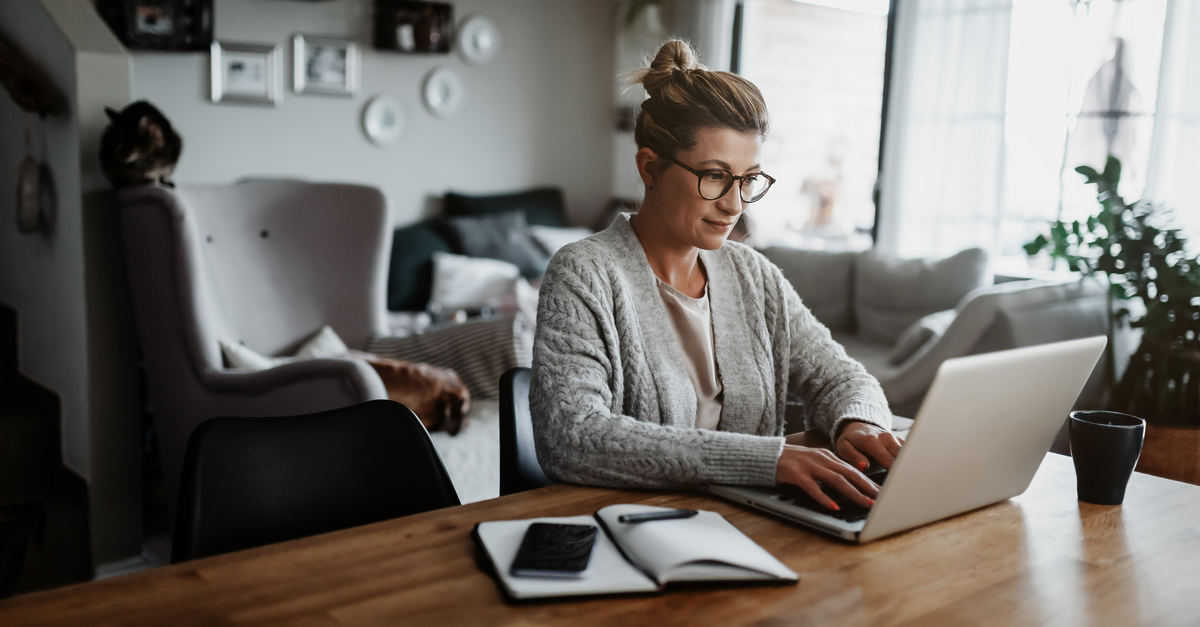 A woman wearing glasses is focused on her laptop, engaged in work at a desk.