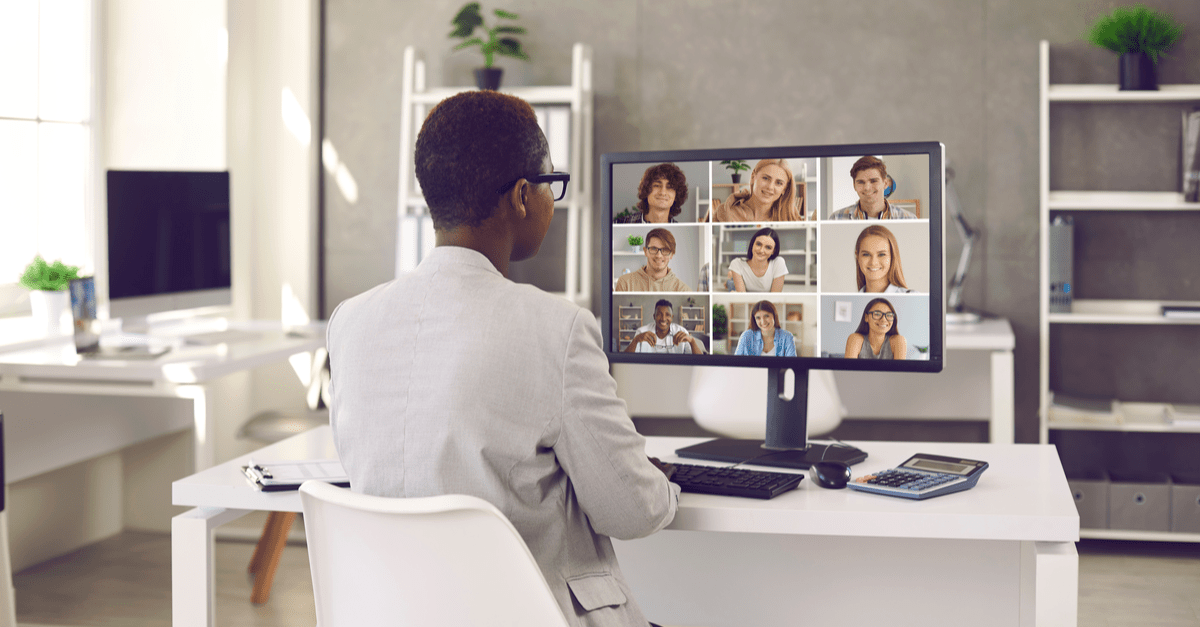 A man sits at a desk, engaging with several people displayed on her computer screen during a virtual meeting.
