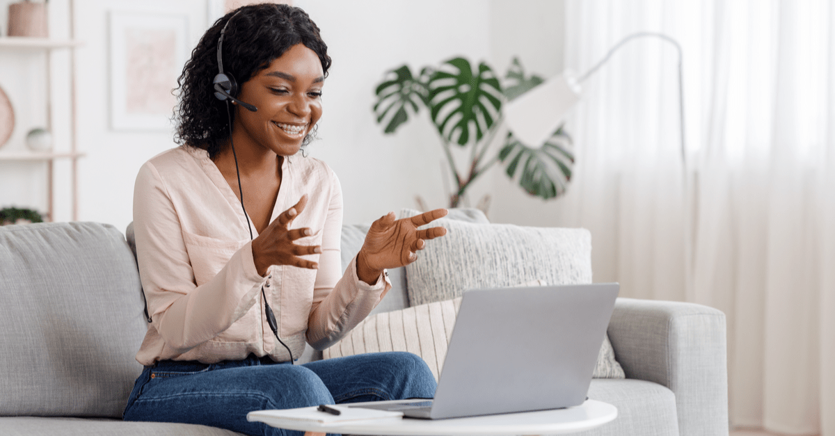 A woman with headphones is seated on a couch, engaged with her laptop in a comfortable indoor environment.