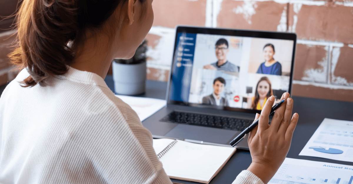 A woman engaged in a video call while using her laptop at a desk, focused and attentive to the screen.
