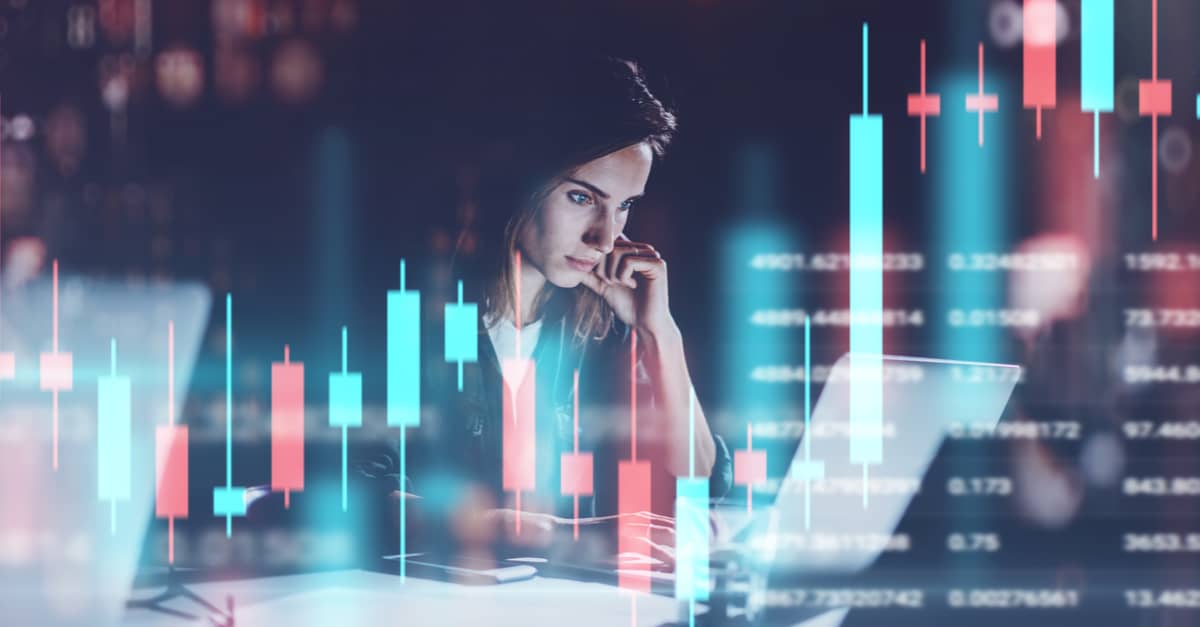 A woman focused on her laptop, analyzing a stock chart displayed on the screen in front of her.