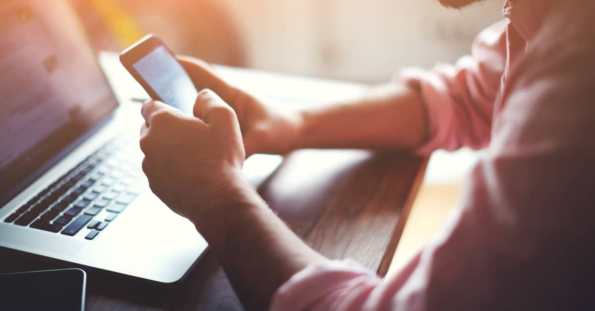 A man sitting at a desk is focused on his phone, engaged in a conversation or browsing content.