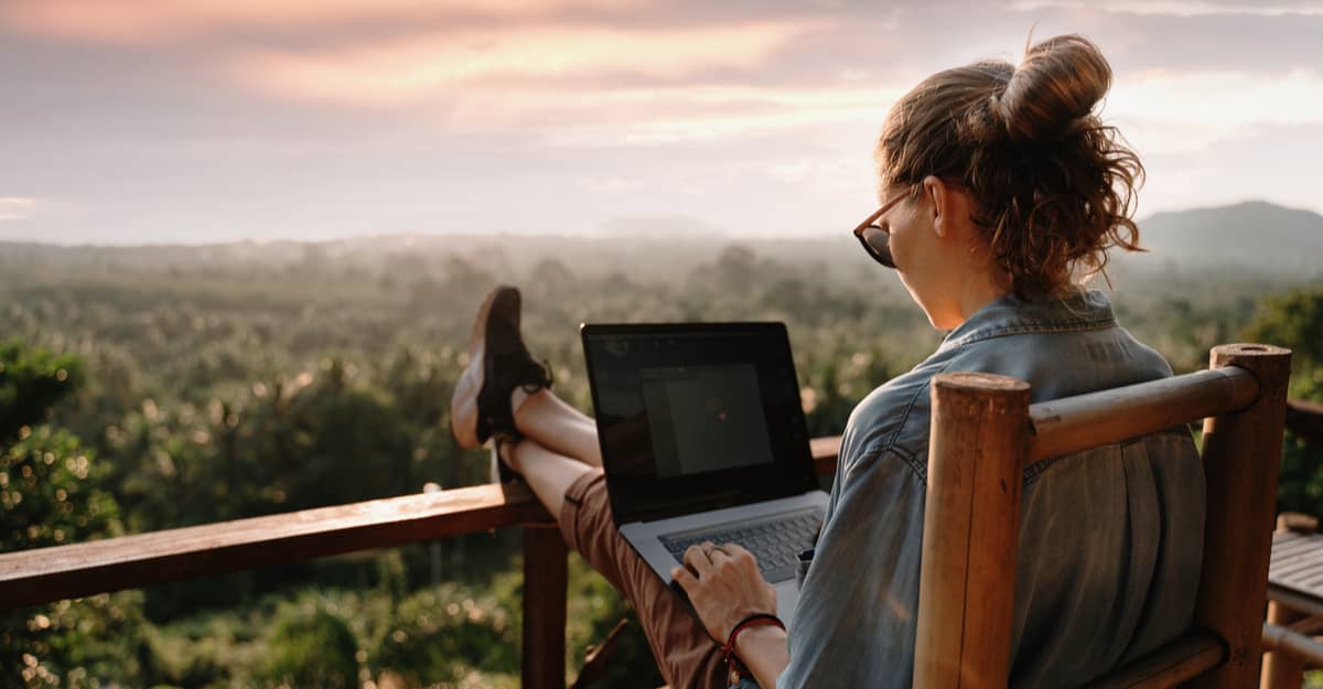A woman using a laptop while sitting on a wooden chair, focused and engaged in her work.