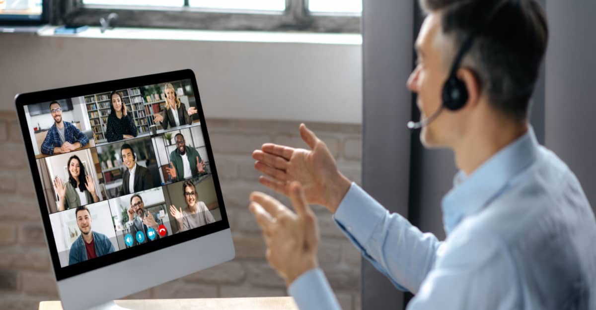 A man in a headset speaks to a group of people displayed on a computer screen during a virtual meeting.