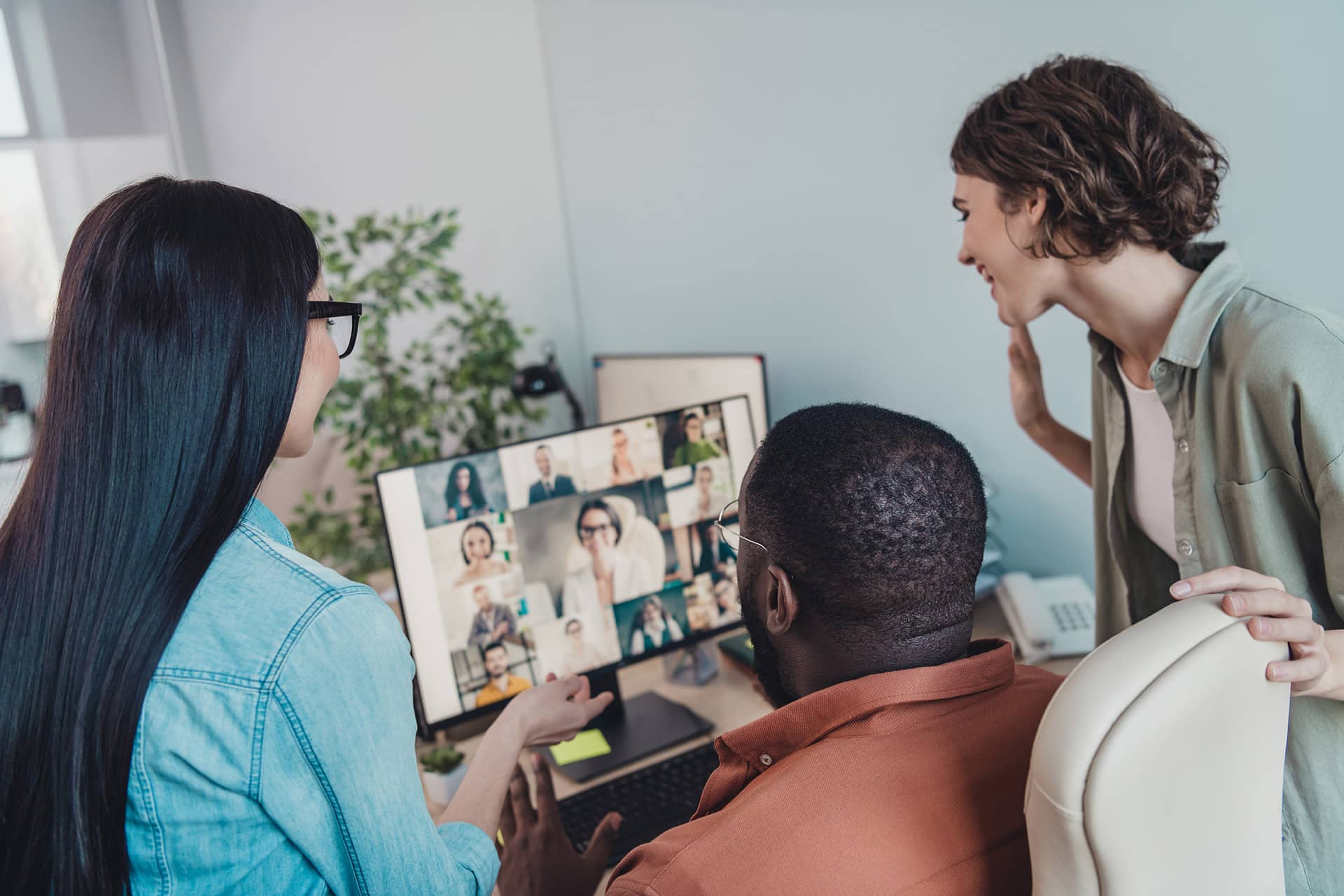 Three colleagues at a desk, attentively looking at a computer screen during a discussion.