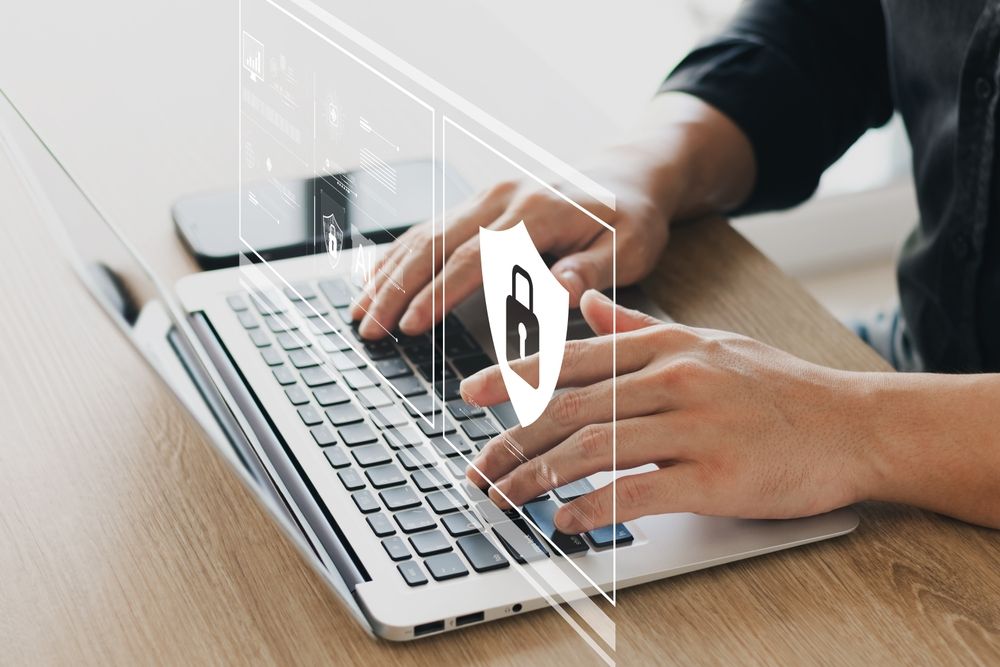 Individual using a laptop with a visible security symbol, emphasizing the importance of secure online practices.