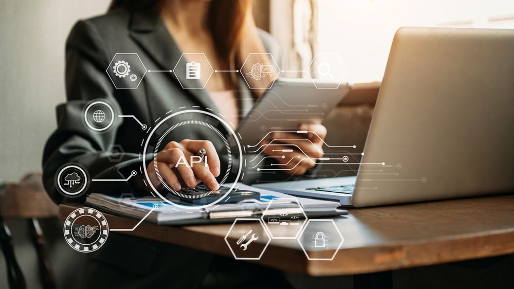 Businesswoman using a laptop and tablet, surrounded by API icons representing various business concepts.