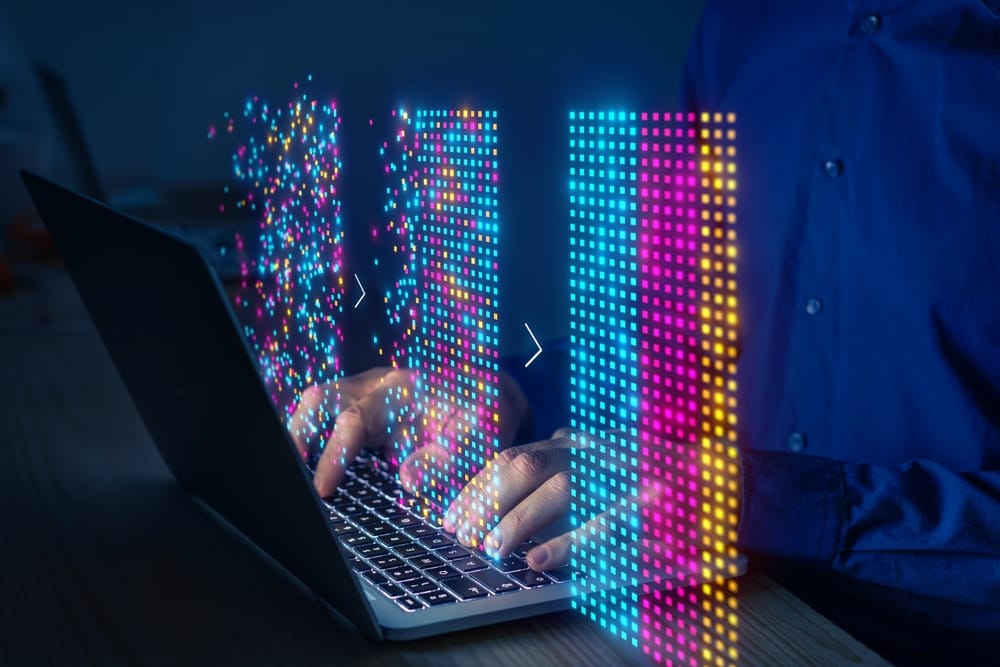 A person engaged in typing on a laptop, with an array of colorful pixel graphics surrounding them.